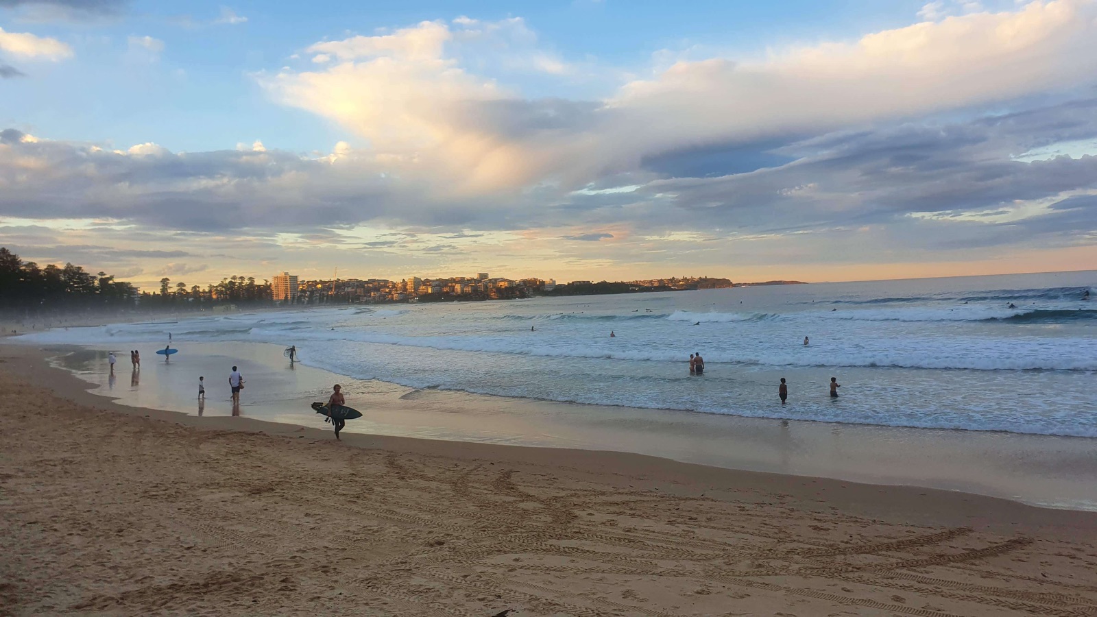 Surfers and swimmers on Manly Beach at sunset