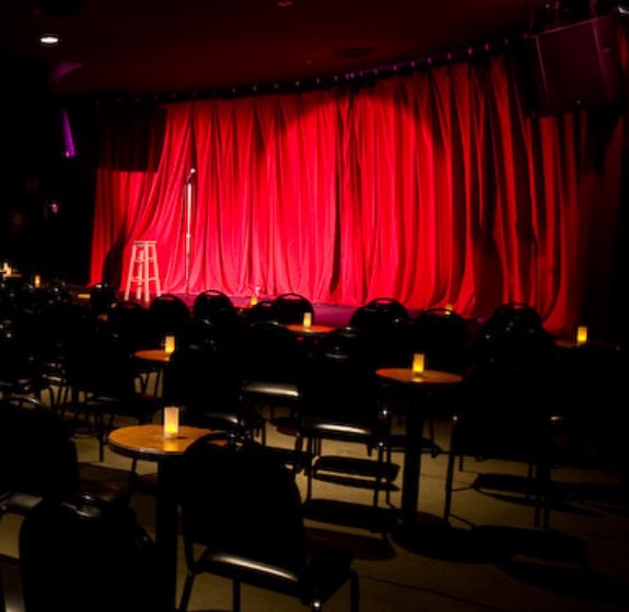 Red-curtained stage, mic stand and candlelit cabaret tables inside The Comedy Store, Moore Park