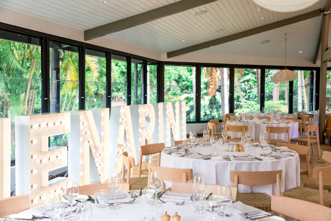 Botanic House dining room set with round tables for a corporate event, gardens beyond the windows