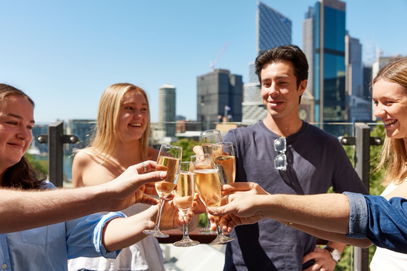 Friends toasting with sparkling wine on The Glenmore's rooftop with the city skyline behind