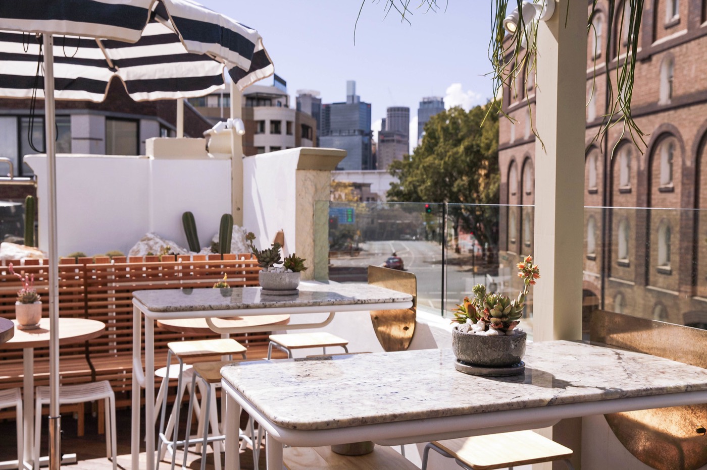 Marble tables and striped umbrellas on the Quarryman's rooftop with city towers behind