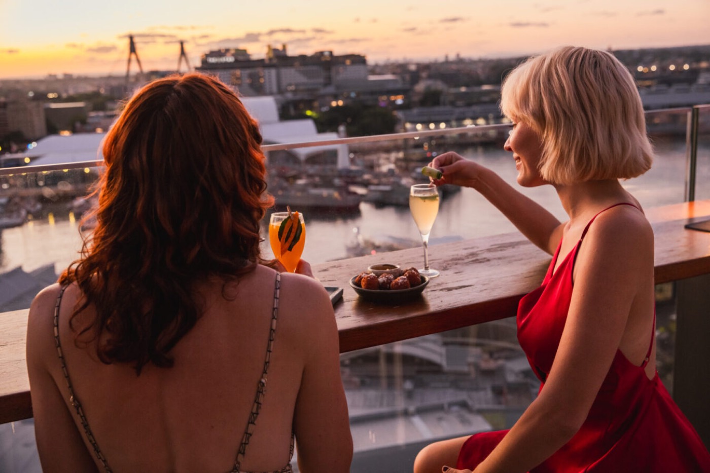 Two women with drinks at Zephyr Bar overlooking Darling Harbour at sunset