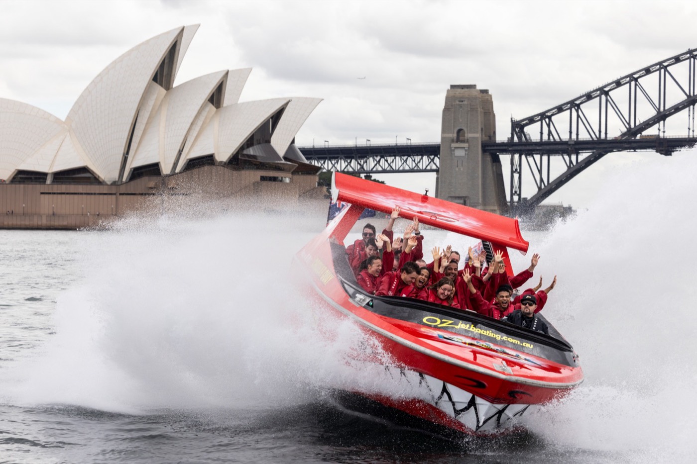 Red jet boat spraying water as it spins in front of the Opera House and Harbour Bridge