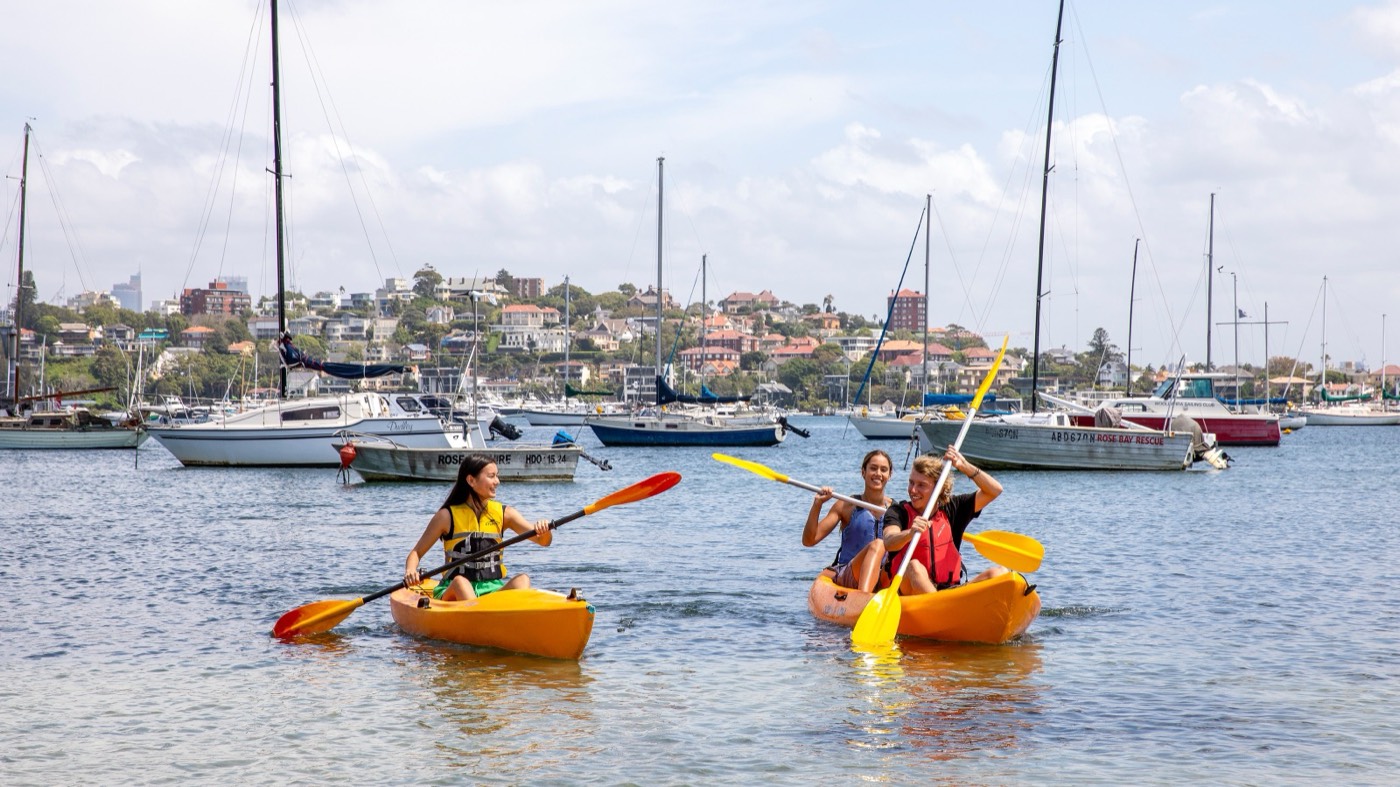 Kayakers paddling past moored yachts in a calm Sydney Harbour bay