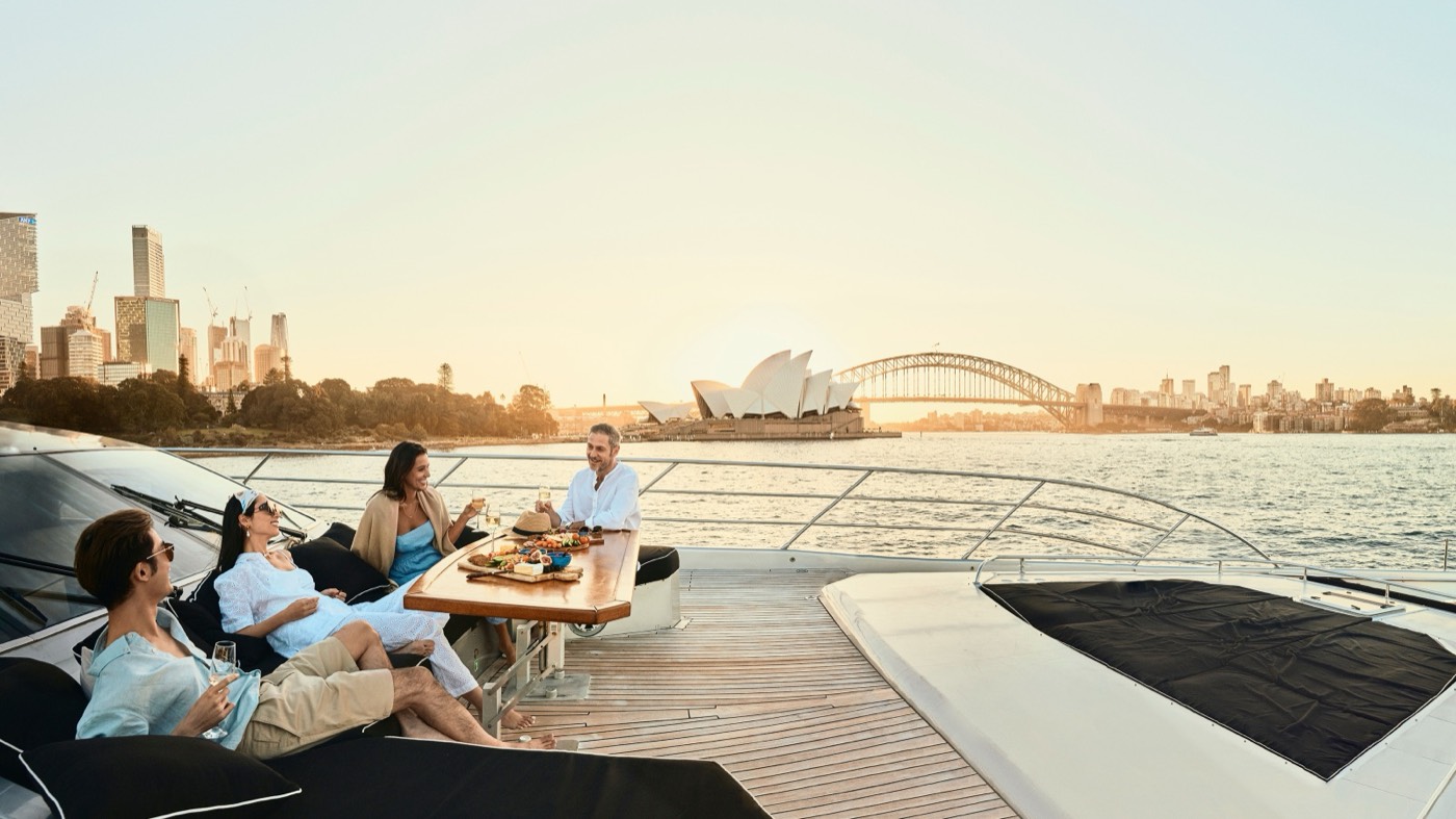 Guests relaxing on the deck of a private yacht with the Opera House and Harbour Bridge behind