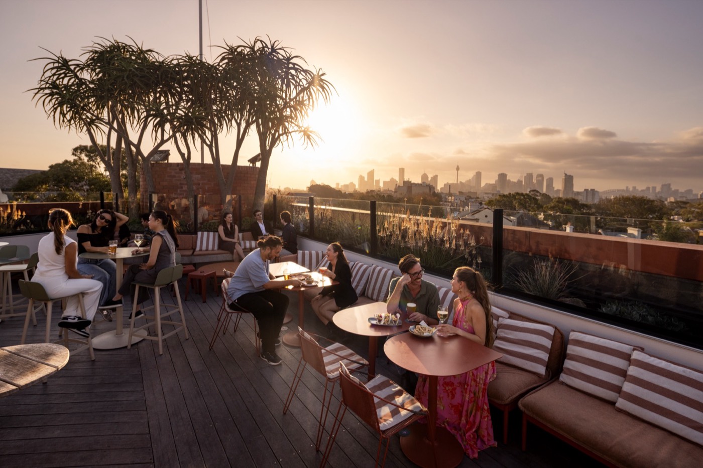 Guests at tables on a Sydney rooftop bar terrace at golden hour