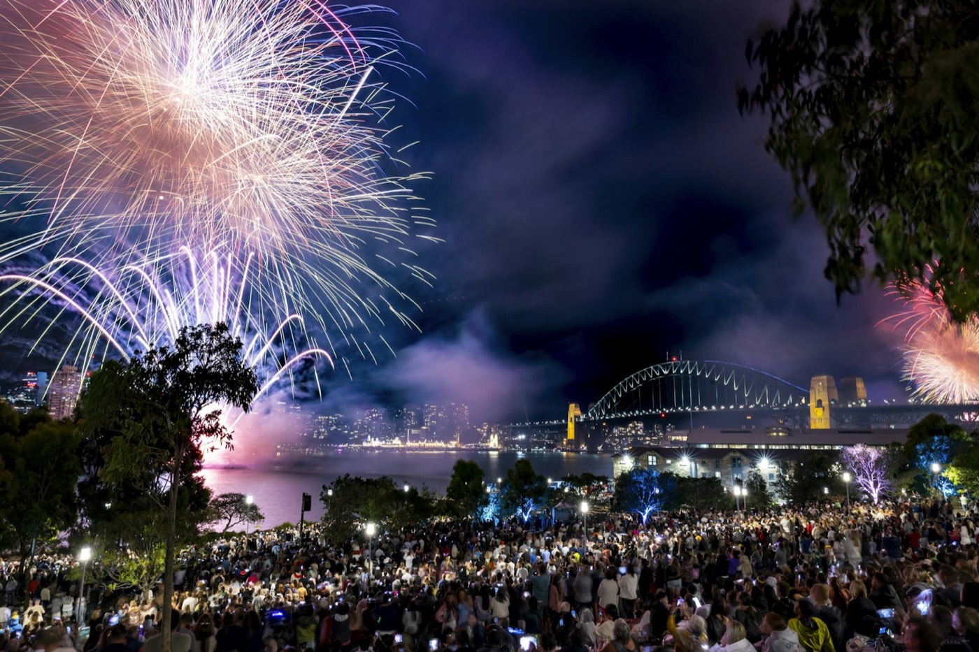 Fireworks bursting above a large crowd at Barangaroo Reserve with the Harbour Bridge behind