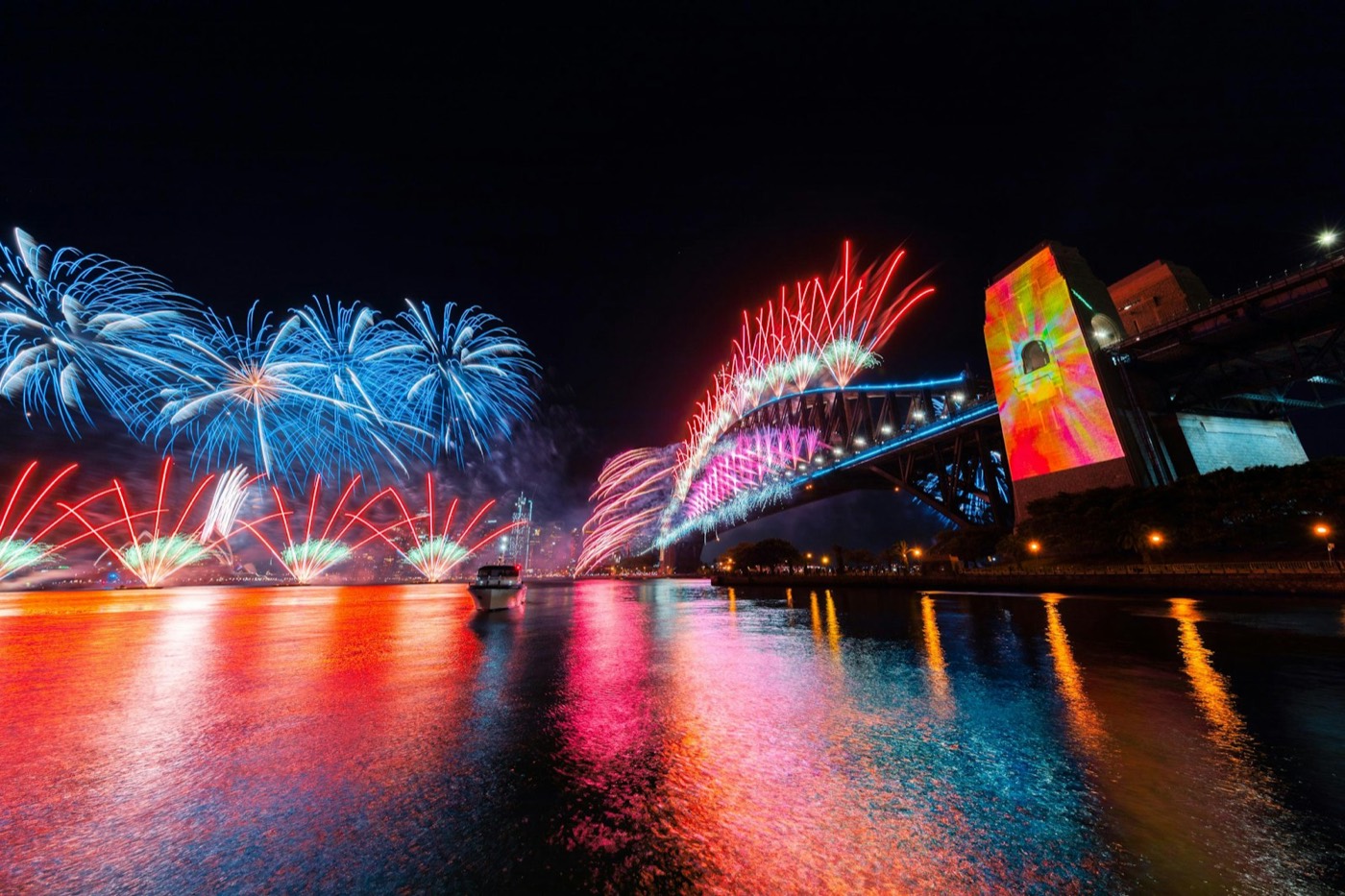 Blue and red fireworks firing from the Harbour Bridge and reflecting on the water at night