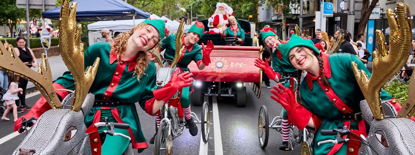 Elves on reindeer tricycles riding ahead of Santa's sleigh along a Sydney street