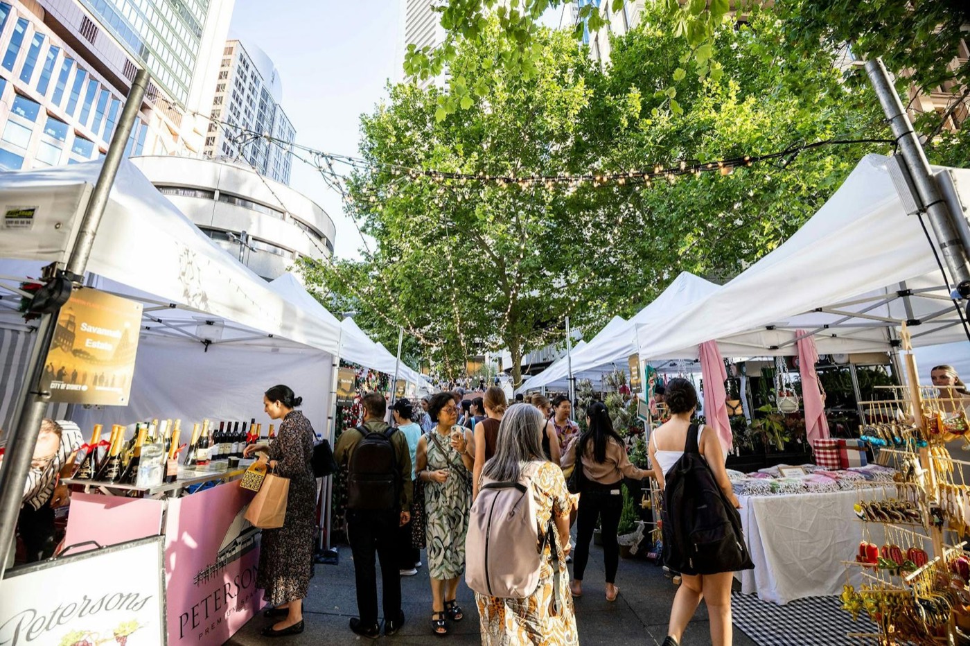 Shoppers browsing white-tented market stalls under the trees in Martin Place
