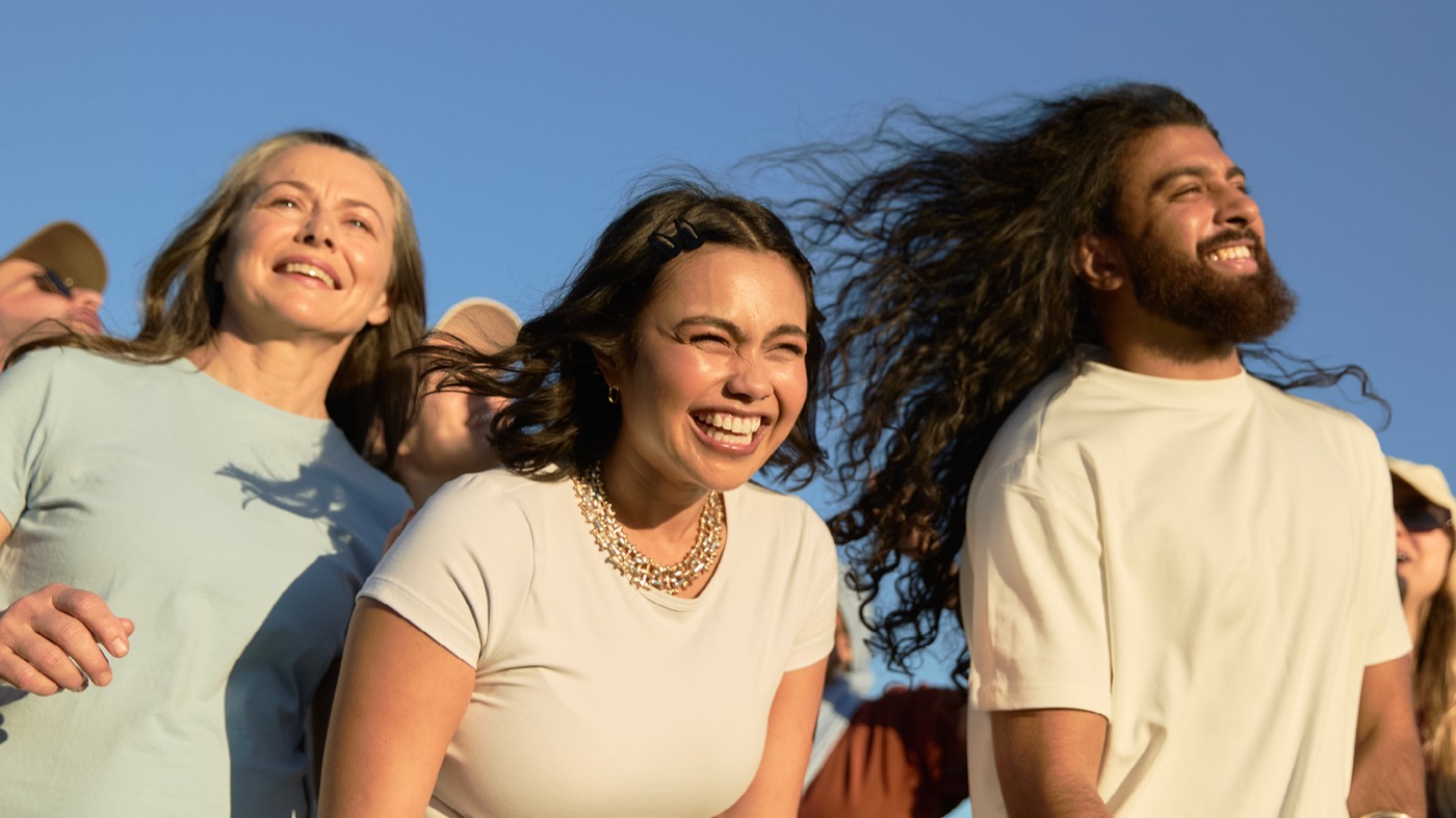 Three smiling festival-goers with wind-blown hair under a blue summer sky
