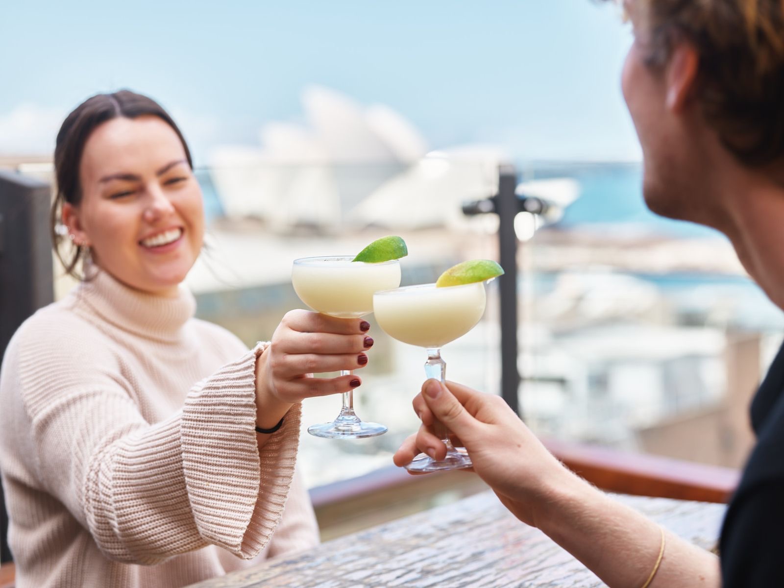 Couple toasting cocktails on The Glenmore rooftop with the Opera House behind