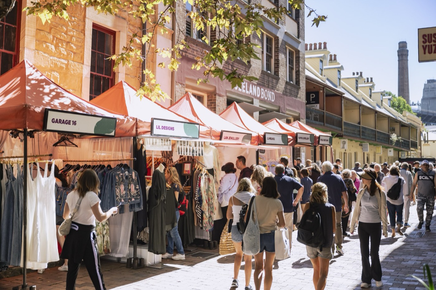 Shoppers browsing market stalls on a sandstone street at The Rocks Markets