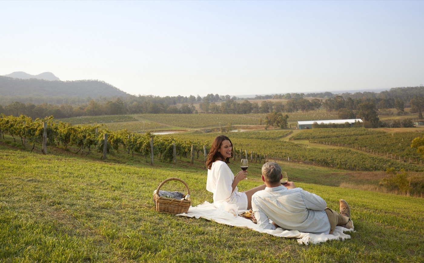 Couple picnicking with wine above vineyard rows in Pokolbin, Hunter Valley