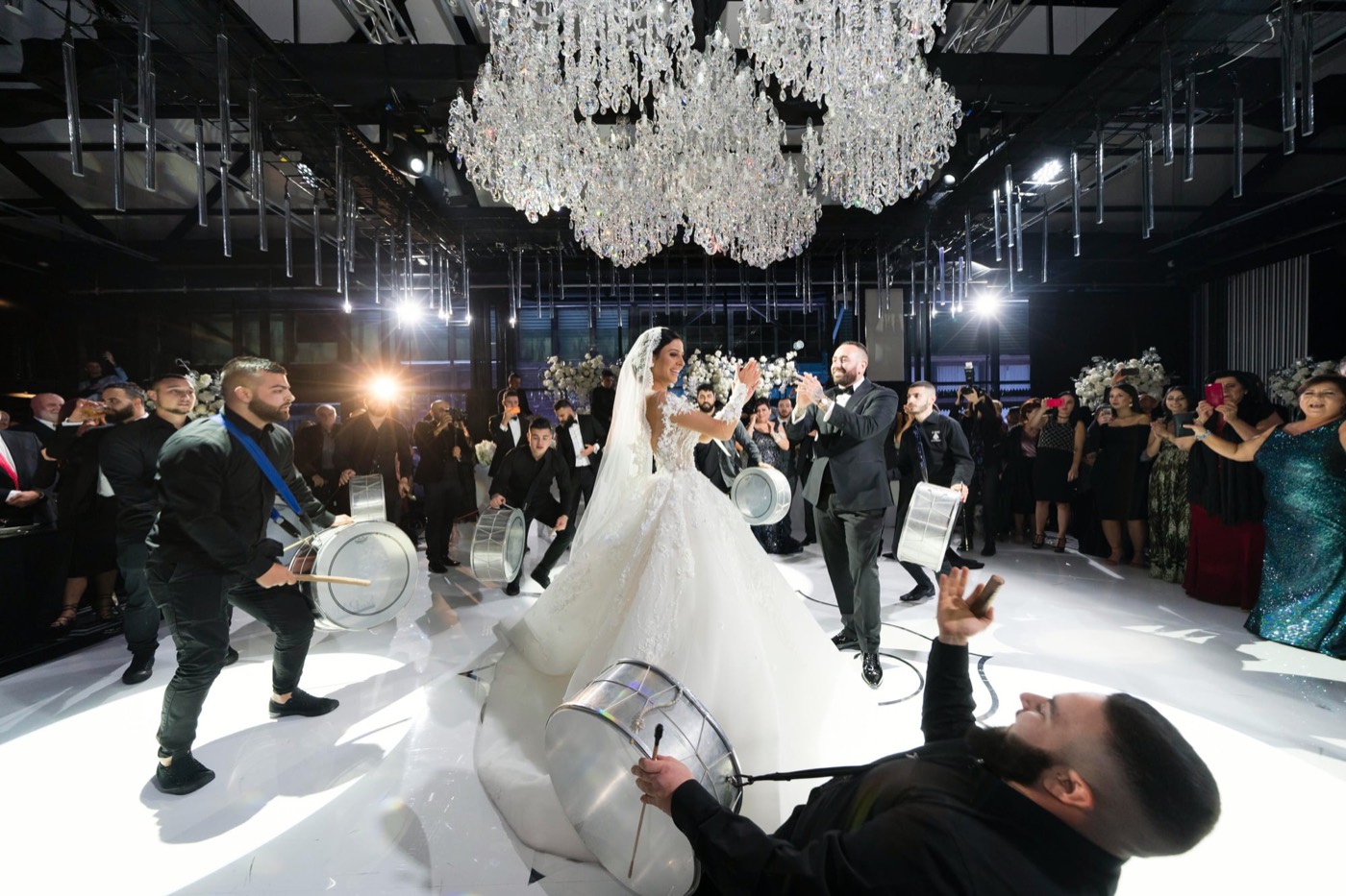 Bride and groom dancing with drummers under crystal chandeliers at a Doltone House reception
