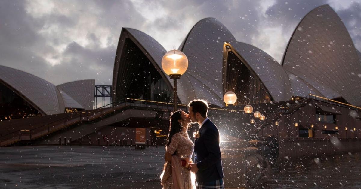 Newlyweds kissing in the rain beneath the Sydney Opera House sails at dusk