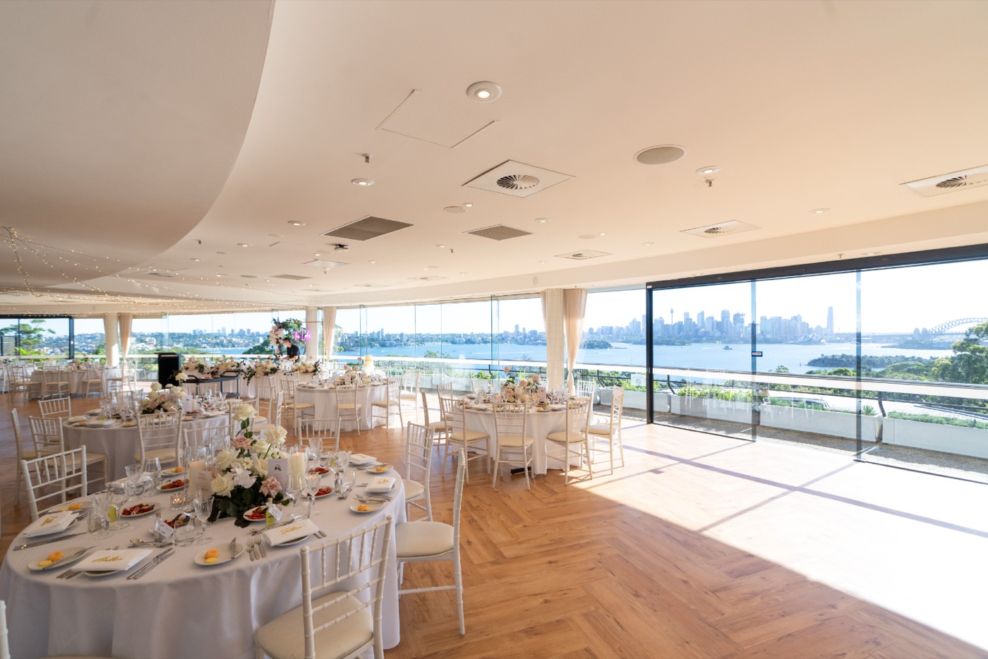 Wedding reception tables in a Taronga function room with floor-to-ceiling harbour and city views